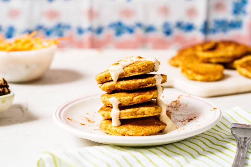 Mini Carrot Cake Pancakes with Vanilla Greek Frosting from Holley Grainger - Image of five cakes stacked on a white plate with icing drizzle